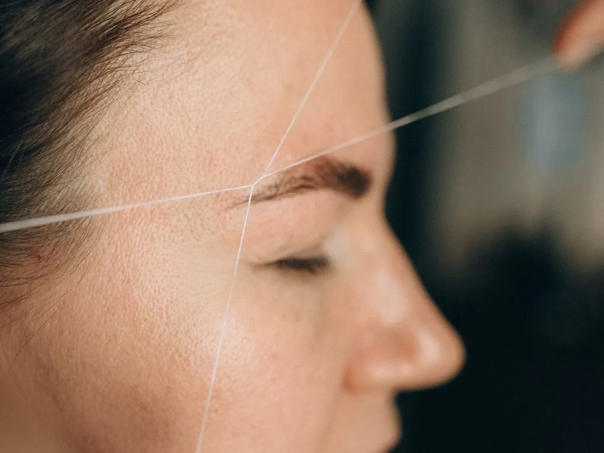 Eyebrow threading with a cotton thread, close-up